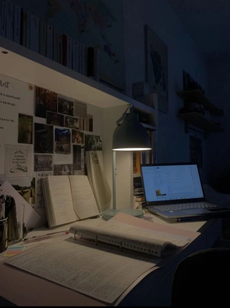 a desk late at night, a single lamp over open notebooks and a laptop